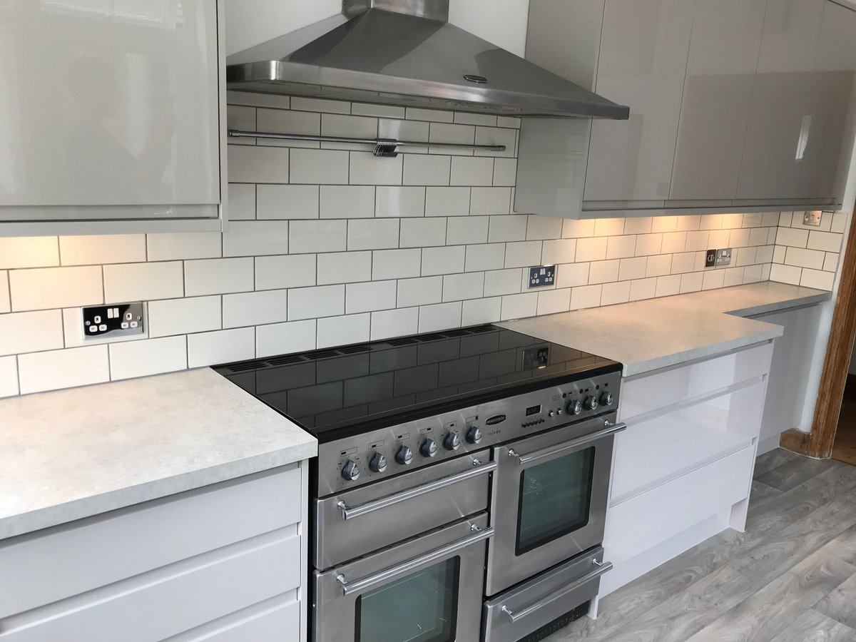 Modern kitchen with white cabinetry, stainless steel dual range cooker, black countertops, and white subway tile backsplash with steel hood vent
