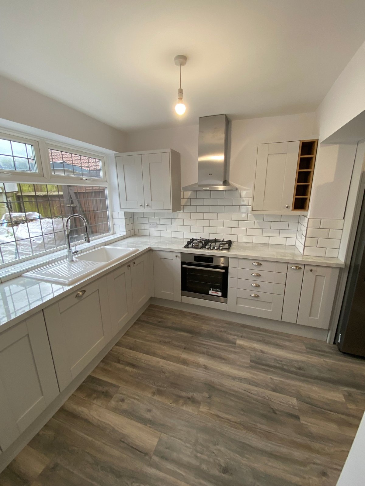 Modern white kitchen with gas stovetop, stainless steel hood, subway tile backsplash, and wood-look flooring