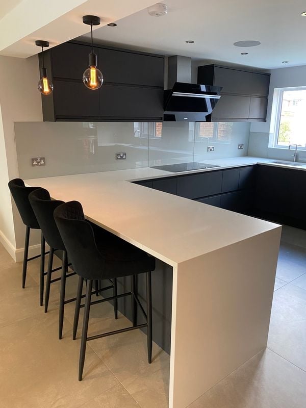 Modern kitchen with white island countertop, black bar stools, dark cabinetry, glass backsplash, and pendant lights