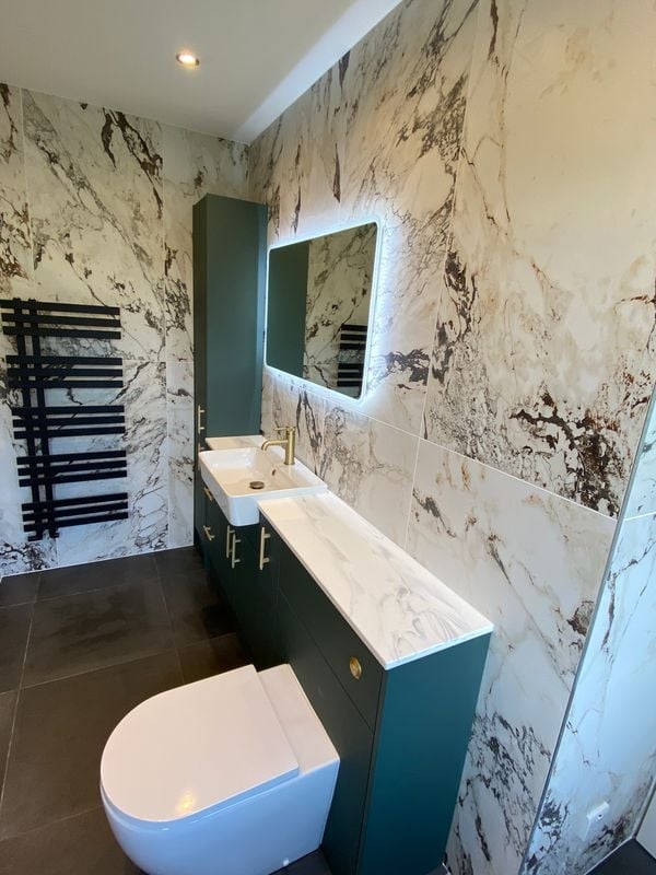 Modern bathroom with marble-effect walls, white toilet, teal vanity with sink, and LED-lit mirror